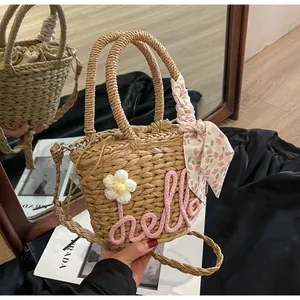 Detail of woven straw bucket bag with pink hello embroidery and floral silk scarf accessory