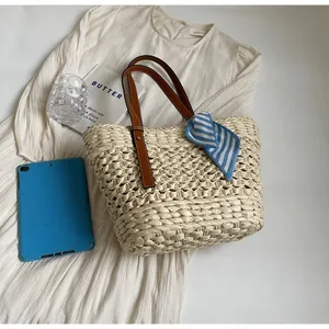 Detail of woven straw tote bag with brown leather handles and striped silk scarf decoration