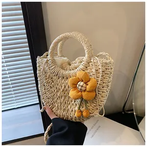 Dettaglio borsa in paglia beige con manico rotondo e ciondolo a fiore giallo