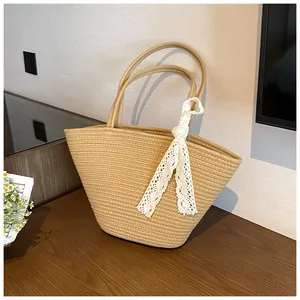 Close-up of a hand-woven straw tote bag with delicate white lace ribbon on a wooden table