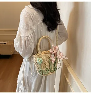 Detail of straw woven handbag with hello embroidery and floral ribbon on a model