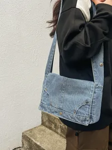 Vintage Jeans-Umhängetasche in Hellblau mit Nieten und breitem Trageriemen am Model