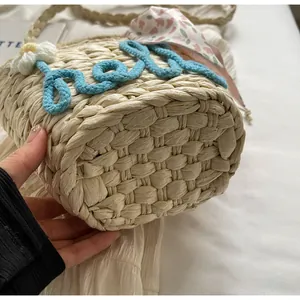 Detail of woven straw bag bottom with blue Hello rope embroidery and floral silk scarf