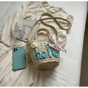Detail of woven straw bag with blue hello text, white daisy and floral silk scarf
