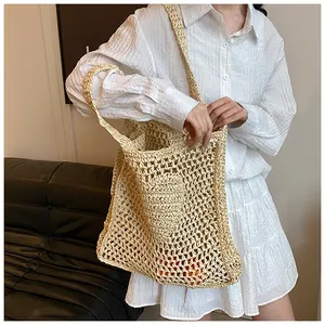 Detail of hollow-out straw tote bag with heart charm on a shoulder-worn model