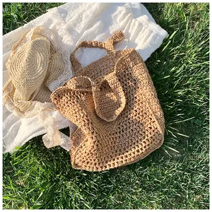Detail of hollow woven straw tote bag with lace-trimmed beach hat on green grass
