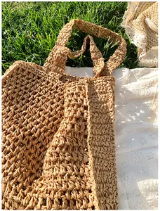 Detail of hollow woven straw tote bag in khaki on grass for beach or travel use