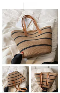 Detail view of woven straw tote bag with black stripes and brown leather handles