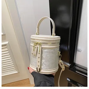 Detail of floral embroidery on cream cylinder bucket bag with gold zipper and hardware