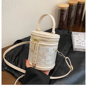 Detail of floral embroidery on a beige cylinder bag with gold hardware and strap