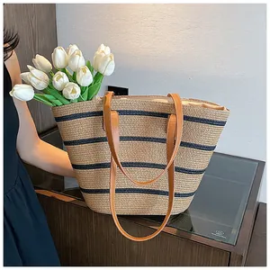 Detail of woven straw tote featuring navy blue stripes and brown faux leather straps