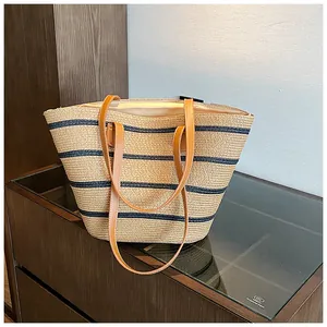 Detail of the woven straw tote bag featuring black stripes and brown leather straps
