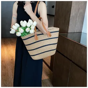 Detail of large straw tote with navy stripes and brown leather straps for beach holidays