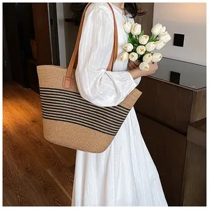 Detailed close-up of woven straw tote bag with black stripes and brown leather straps