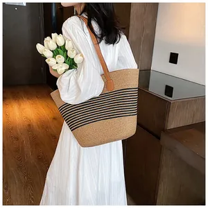 Detail of a large straw tote bag with black stripes and brown leather shoulder straps