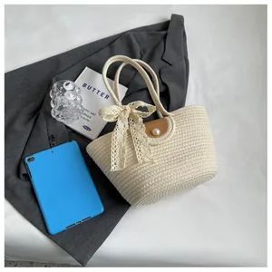 Détail du sac tissé blanc cassé avec nœud en dentelle blanche et bouton en perle