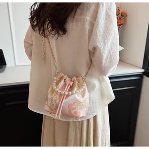 Detail of pink satin bucket bag with gold floral embroidery and pearl handle strap
