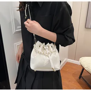 Detail of white satin bucket bag with floral embroidery and pearl handle on model