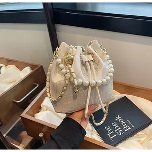 Detail of beige drawstring bucket bag with floral embroidery and pearl handle strap
