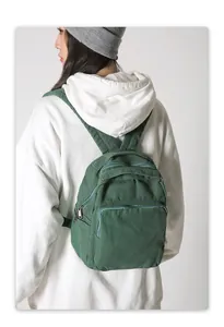 Detalle de la mochila de lona verde bosque usada en la espalda por modelo en blanco