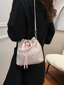 Pink jacquard bucket bag with pearl handle worn as crossbody on black outfit