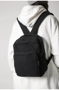 Vista trasera de una modelo con mochila minimalista de lona negra y bolsillo frontal