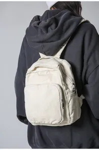 Detalle de mochila de lona crema con cremalleras y múltiples bolsillos sobre modelo