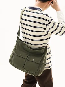 Large military green canvas messenger bag worn by a model in a casual workwear style