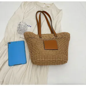 Vue à plat d'un sac cabas en paille tressée avec bandoulière et écusson en cuir brun