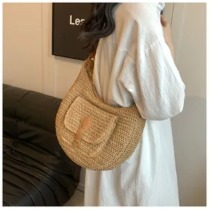 Detail of hand-woven straw hobo bag with brown faux leather strap and front pocket detail