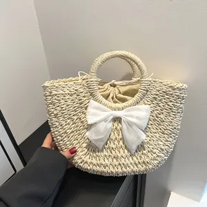 Gros plan sur un sac en paille beige avec un grand nœud en satin blanc et une anse ronde