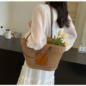 Détail du sac cabas en paille tressée avec anses en cuir marron porté sur une robe
