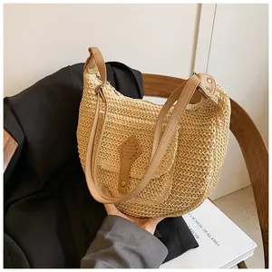 Detailed close-up of straw woven texture and brown leather strap on a beige saddle bag