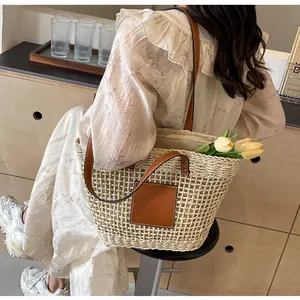Détail d'un sac cabas en paille tressée avec poignées en cuir marron et un empiècement carré