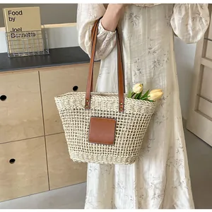 Détail d'un sac cabas en paille tressée avec anses en cuir marron et écusson