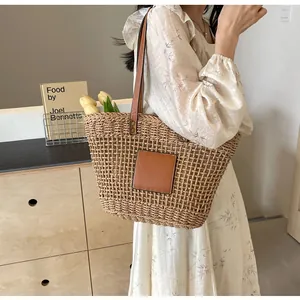 Détail d'un sac fourre-tout en paille tissée avec anses en cuir brun porté à l'épaule