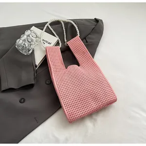 Detalle de bolso de punto rosa con diseño de malla hueca y asa de cadena de perlas