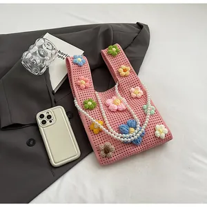 Detalle de bolso tipo cubo de punto rosa con flores de colores y correa de perlas