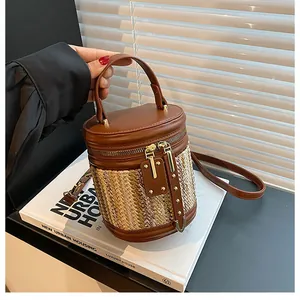 Detail of a woven bucket bag featuring brown leather trim and dual metal zippers
