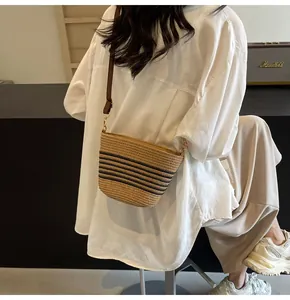 Detail of woven straw crossbody bag with black stripes and brown faux leather strap