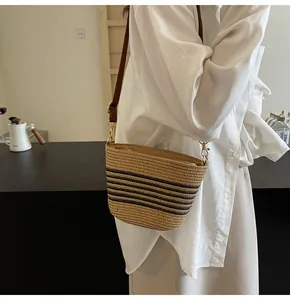 Detail of woven straw shoulder bag featuring black stripes and brown leather strap