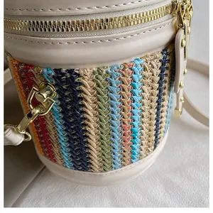 Detail of colorful woven straw bucket bag with off-white leather trim and gold zipper