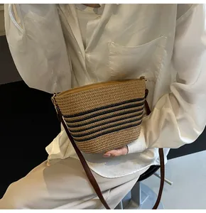 Close-up of handwoven straw bucket bag with black stripes and brown leather strap
