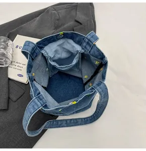 Détail du sac cabas en jean bleu avec broderie florale, poche interne et bouton aimanté