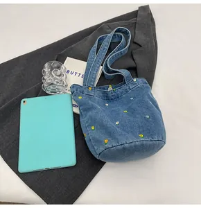 Détail d'un sac seau en jean bleu avec broderies florales et larges bandoulières