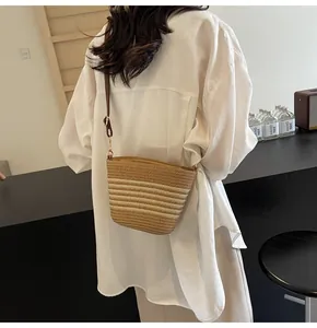 Detail of woven straw bucket bag with gradient stripes and brown leather strap on model