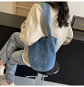 Détail des broderies florales sur un sac cabas en denim bleu porté par un mannequin