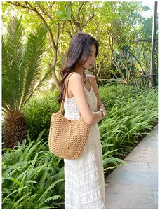 Outdoor shot of a woven straw tote bag paired with a white dress for a summer beach look