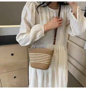 Detail of striped woven straw crossbody bag featuring brown leather strap and metal buckle