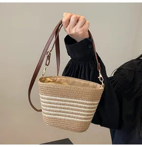 Detail of woven straw striped bucket bag with leather strap and metallic hook